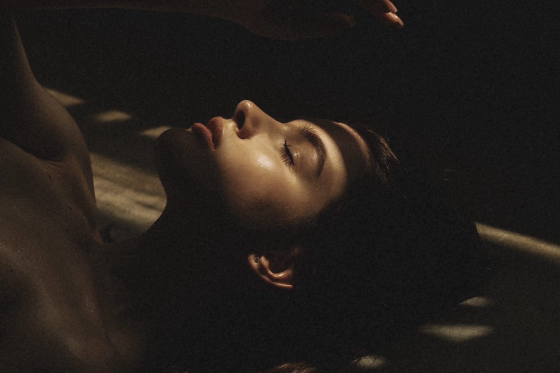 Low-key portrait of a woman with closed eyes lying in soft window light